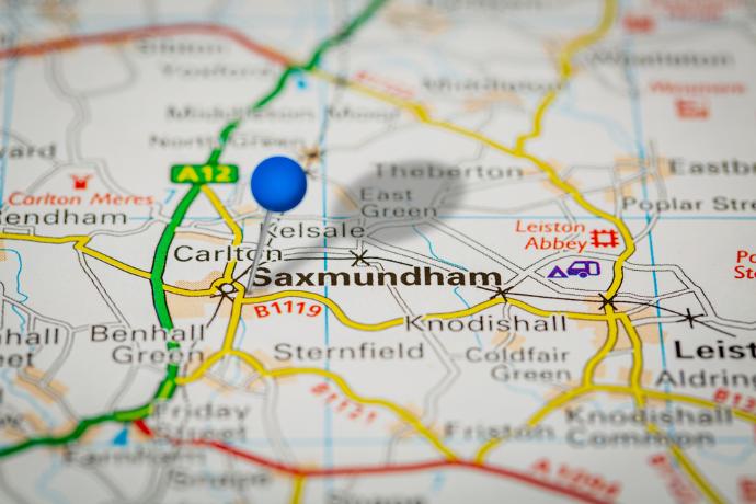 A close up on a colourful printed map with a blue pin stuck in the map at Saxmundham. 